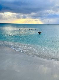 Scenic view of sea against sky during sunset with woman in water