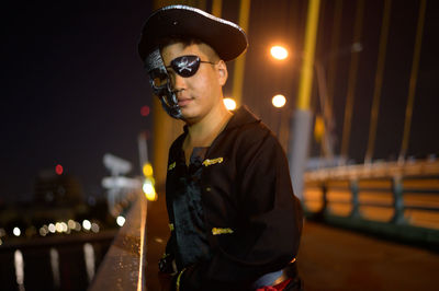 Portrait of young man wearing pirate costume standing on bridge at night