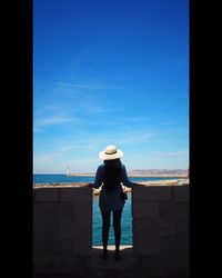 Rear view of woman standing on beach against blue sky