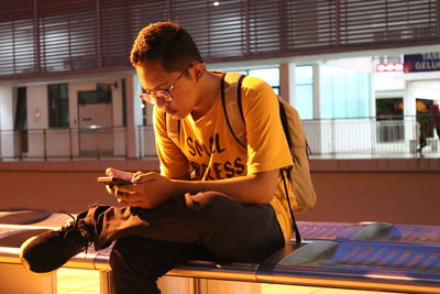 Young man using smart phone while sitting on laptop