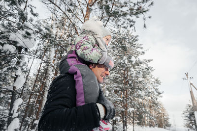 Cheerful father and daughter on shoulders walking in the winter forest