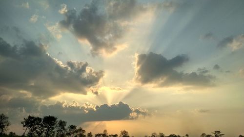 Low angle view of sunlight streaming through clouds during sunset