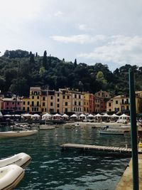 Boats moored in river by buildings against sky