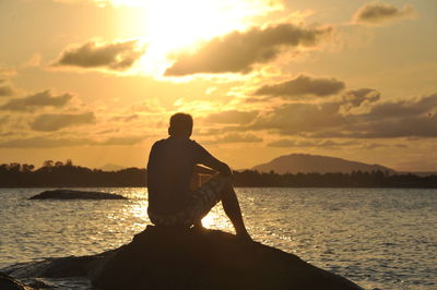 Rear view of man on sea against sky during sunset