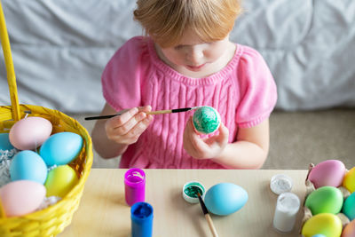 Little girl in easter bunny ears painting colored eggs. easter at home and craft concept.