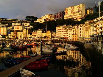 Boats moored at harbor against sky in city