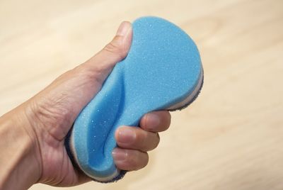 Cropped hand of man holding sponge over wooden table