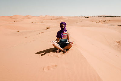 A man in a turban meditating on a dune in the sahara desert