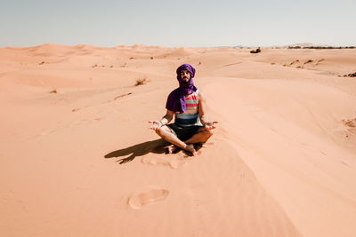 Full length of man sitting on sand dune