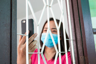 Portrait of man holding camera while standing by window