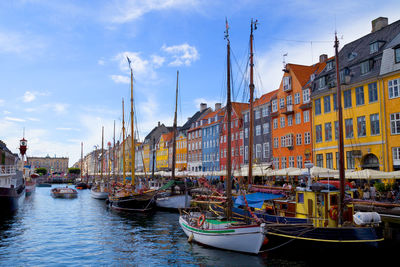 Boats moored in canal by buildings against sky