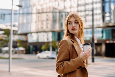 Portrait of young business woman wearing camel color coat. walking in street of european city.