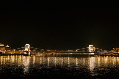 Illuminated bridge over river against sky at night