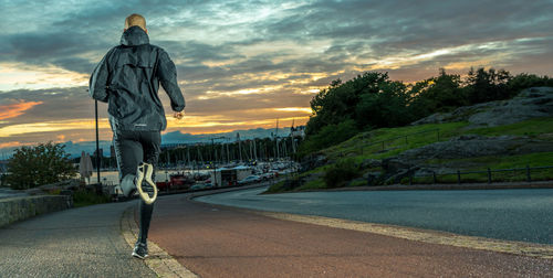 Rear view of man running on road against cloudy sky during sunset