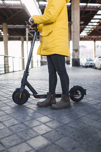 Young woman in yellow coat prepares and uses her electric skateboard.