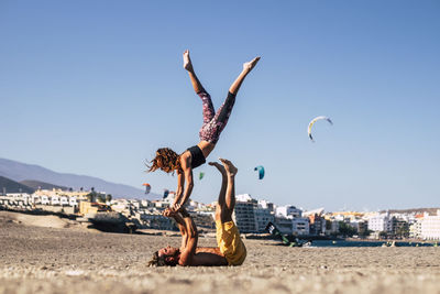 Couple exercising on beach against clear sky