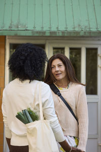 Female friends standing in front of wooden house and talking together