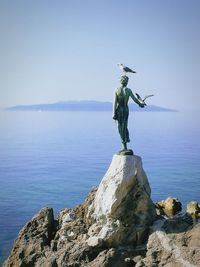 Statue on rock by sea against clear sky