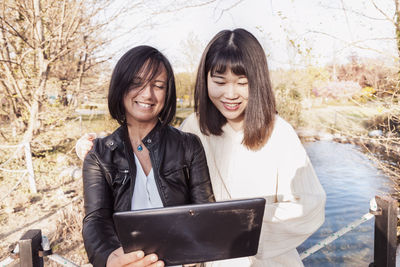 Smiling colleague holding digital tablet standing at park