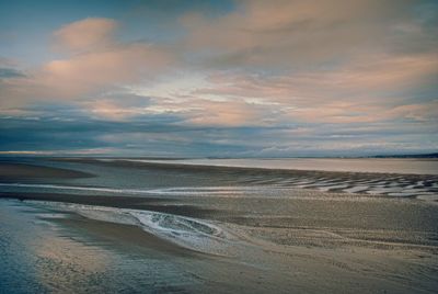 View of calm beach against cloudy sky