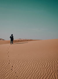 Rear view of man walking on sand dune in desert