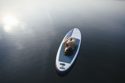 Woman lying in embryo pose on paddleboard at sunset