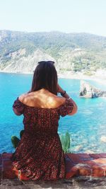 Rear view of woman looking at sea while sitting on cliff