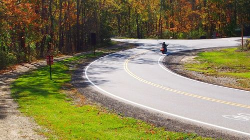 Man riding motorcycle on road in forest during autumn