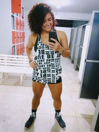 Full length portrait of young woman using phone while standing on tiled floor