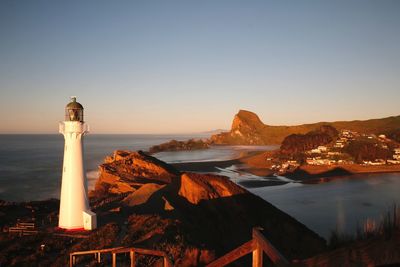 Lighthouse by sea during sunset