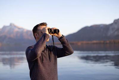 Man looking through binoculars by lake