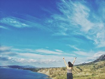 Rear view of woman with arms raised against sky