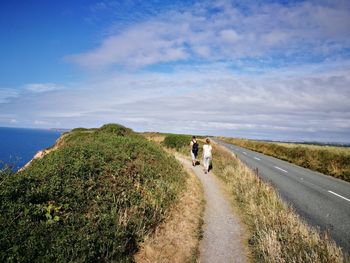 Rear view of people walking on road against sky