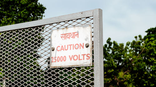 Warning information sign on metal fence against sky