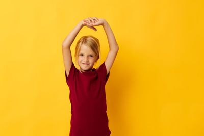 Young woman with arms raised standing against yellow background