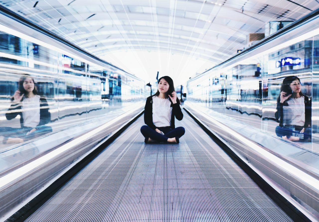 one person, looking at camera, adults only, only women, full length, front view, portrait, real people, women, one woman only, people, indoors, adult, young adult, moving walkway, commuter, day, futuristic, one young woman only