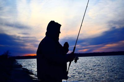 Silhouette man fishing on sea against sky during sunset