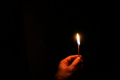Cropped hand of person holding lit matchstick against black background