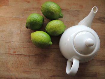 High angle view of limes by teapot on wooden table