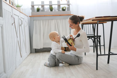 Baby of 10 months together with mom play kitchen utensils, lifestyle in the real interior 