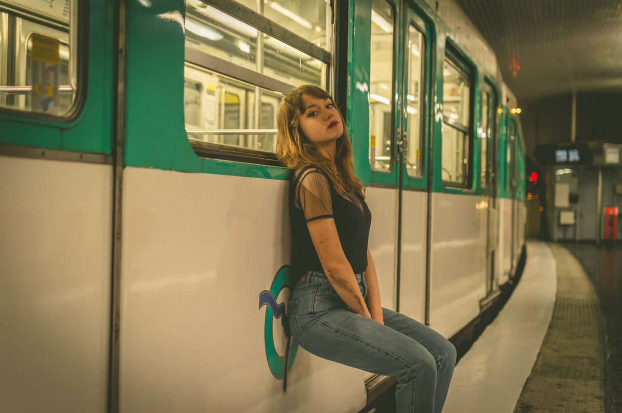 one person, transportation, rail transportation, mode of transportation, train, young adult, women, adult, public transportation, travel, casual clothing, lifestyles, subway train, public transport, commuter, railroad station, architecture, hairstyle, city life, city, subway, vehicle, journey, passenger, railroad station platform, long hair, leisure activity, transport, sitting, motion, emotion, full length, side view, window, metro, land vehicle, female, looking, outdoors, track, smiling, passenger train, portrait, railroad track, on the move