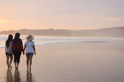 Rear view of women walking on beach during sunset