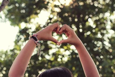 Midsection of woman making heart shape against tree