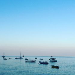 Boats in calm blue sea against clear sky