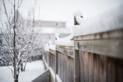 Snow piled high on top of wooden fence in a backyard on a snowy day.