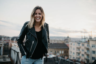 Portrait of smiling young woman standing against sky in city