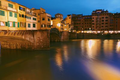 Illuminated buildings by river against sky in city at night