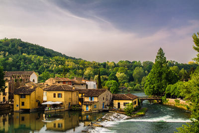 River amidst buildings and trees against sky