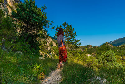 Rear view of woman amidst trees against sky