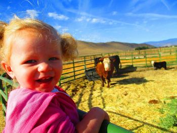 Portrait of cheerful girl standing against cows at farm
